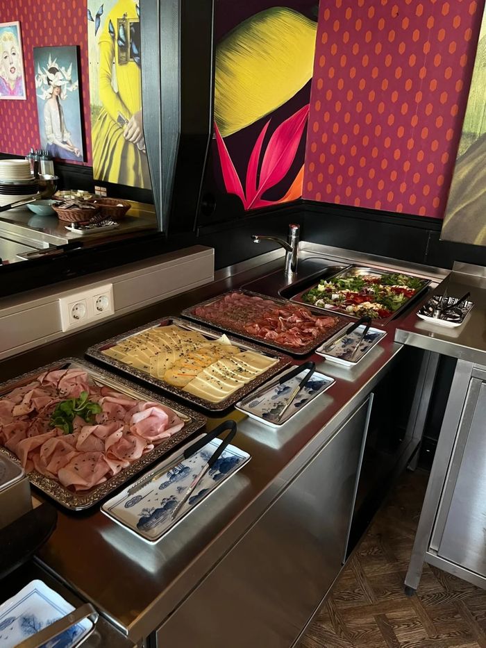 Brunch-Buffet mit Schinken, Käse, Aufstrichen und Salaten vor bunten Kunstdrucken