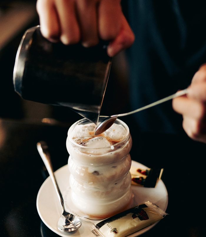 Ein Iced Latte wird mit einem Löffel umgerührt, Milch wird eingegossen