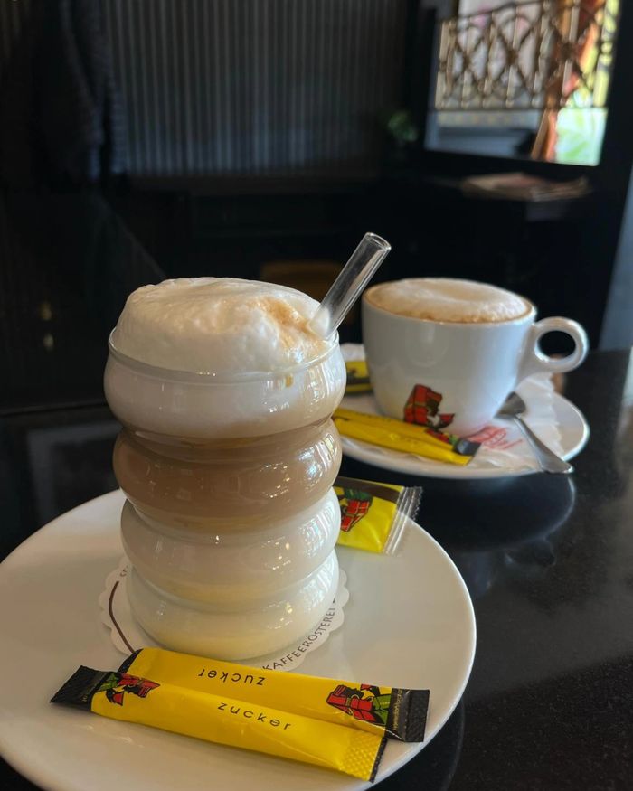 Latte Macchiato in einem geschwungenen Glas mit Strohhalm neben einem Cappuccino