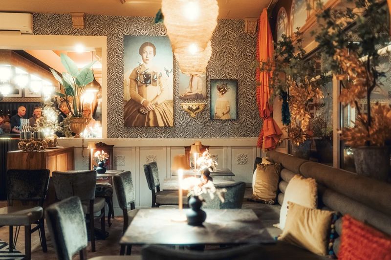 Gastraum des Kunst Café mit Porträtgemälden, Lampions, orangen Vorhängen und gedeckten Tischen